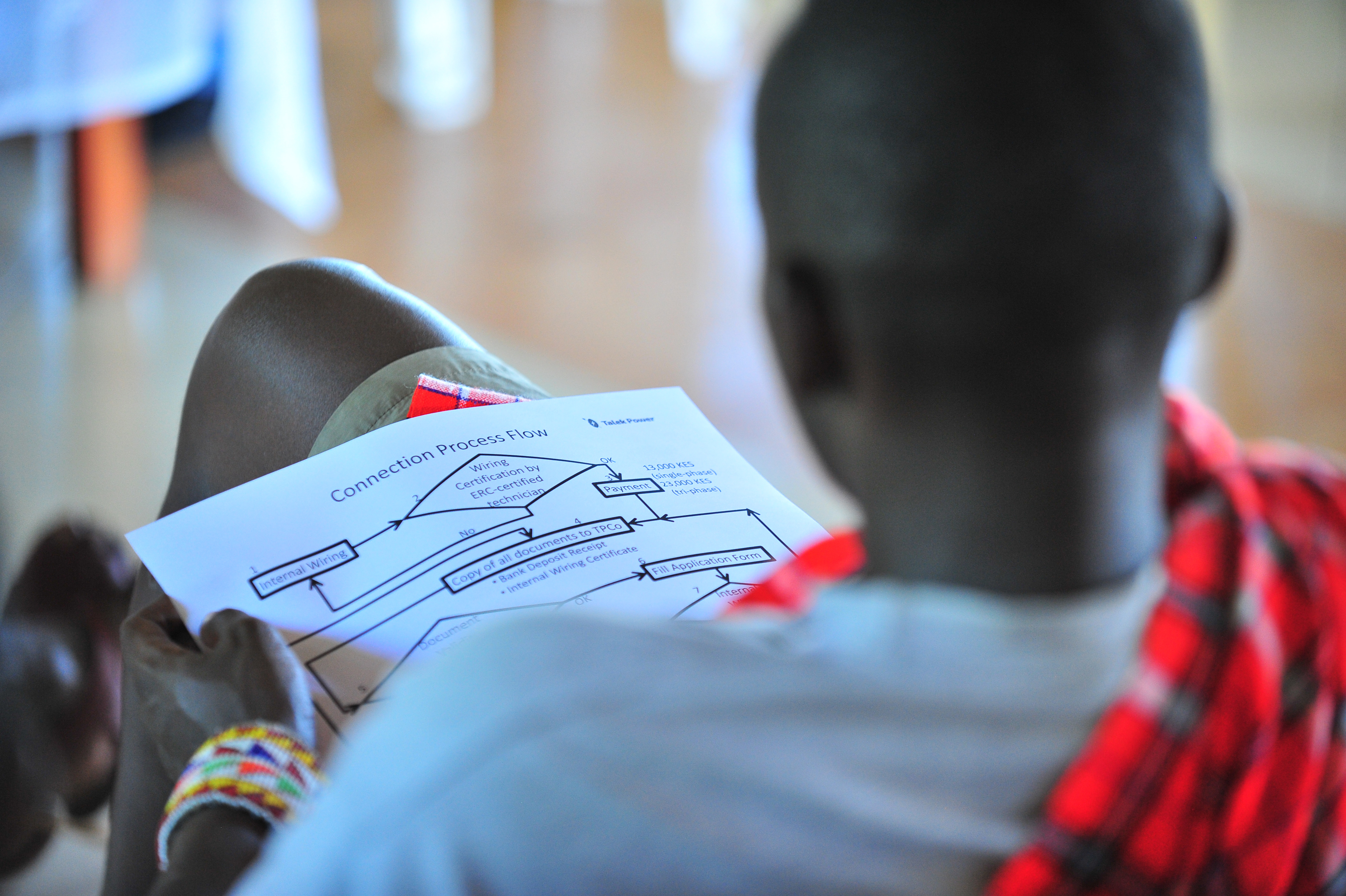 A resident of Talek town reads the Talek Power Company connection process flow chart during a public baraza at AIC Talek to explain how solar power will be connected and distributed in Talek town, Narok County. Through Talek Power, GIZ and other partners have constructed a solar power grid which will connect residents of Talek town in Narok to power for domestic and industrial use.